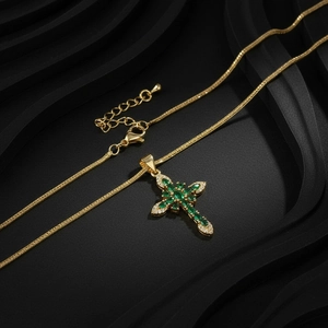 Macro shot of gold cross necklace with green marquise zircon stones and snake chain