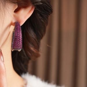 Close-up of model wearing C-shaped earrings with magenta zircon and dark nickel plating