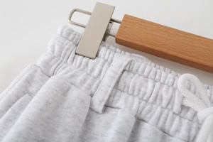 Detail of grey knitted joggers featuring elastic waistband and white drawstring on a hanger