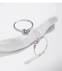 Macro shot of silver drop-shaped rings with blue and pink gems on a stone background