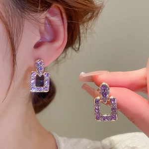 Dettaglio di lussuosi orecchini geometrici quadrati con strass viola e base in lega oro
