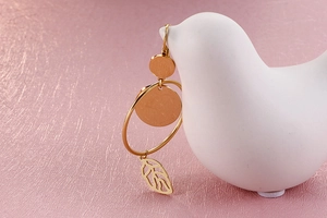 Close-up of gold titanium earrings with leaf pendant on a white ceramic bird stand