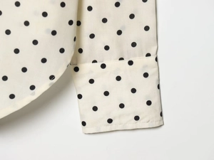 Close-up detail of black polka dots on white long blouse with precise stitching
