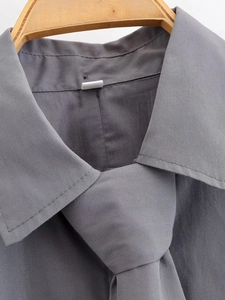 Detail shot of a dark grey cropped shirt neckline featuring a matching tie and sharp collar