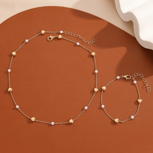 Detail view of gold heart necklace and bracelet set with pearls on a circular display