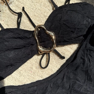 Detail of black textured bikini top with a decorative gold irregular metal ring buckle