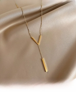 Detailed view of elegant gold Y-shaped necklace with V-pendant on champagne silk fabric