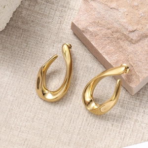 Minimalist gold irregular twisted hoop earrings on textured cloth and pink stone background