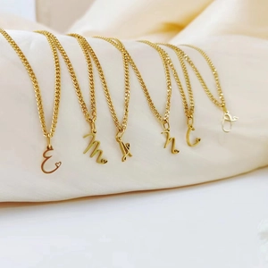 Detailed view of gold stainless steel Cuban necklaces with cursive initial pendants
