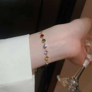 Close-up of colorful zircon gold bracelet on wrist holding a glass in elegant setting