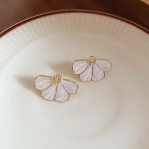 Boucles d'oreilles fleur blanc nacré avec bordure dorée sur un plateau en céramique