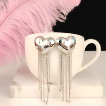 Detail of silver heart-shaped long tassel earrings hanging on a white ceramic cup