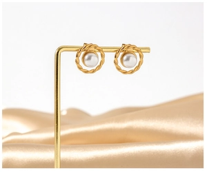 Detail of twisted gold earrings with pearls displayed on a stand over silk fabric