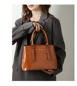 Detail of a brown polished leather tote featuring a trapezoid shape and top handles