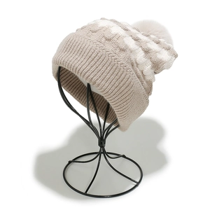 Detail of cable knit pattern and pom-pom on beige and white striped winter hat