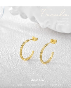Macro shot of gold-plated spiral twist C-hoop earrings on white marble stone surface