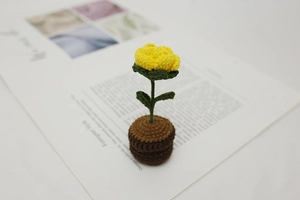 Macro detail of handmade crochet yellow flower in a brown knitted pot on a magazine