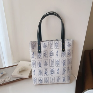 Detail of white canvas tote bag with blue floral patterns and sturdy dark leather straps