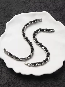 Detail of woven black leather and silver metal chain bracelets on a white ceramic plate