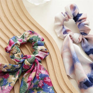 Close-up of floral and tie-dye silk scrunchies with long ribbons on a wooden tray