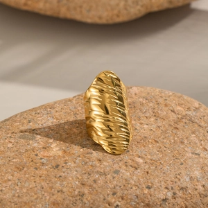Golden textured ring with artistic wavy design displayed on a natural rock surface