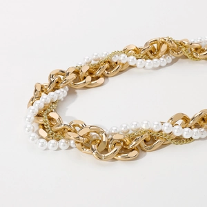 Macro detail of layered gold Cuban chain and white pearls showing premium metallic texture