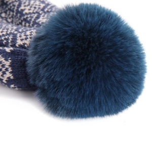 Close-up of a blue knit beanie featuring a large dark teal faux fur pompom detail