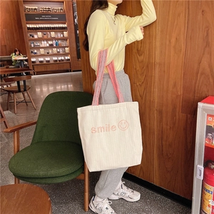 Detailed pink smile embroidery and lace-trimmed strap on a cream canvas tote bag