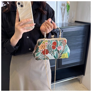 Detail of floral embroidery, golden metal clasp, and pearl handle on a vintage handbag