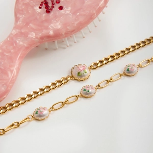 Close-up of gold chain bracelets with vintage floral enamel charms and pink hair comb