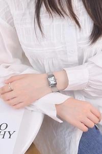 Close-up of rectangular silver stainless steel watch with Roman numerals on wrist