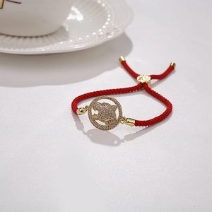 Détail du bracelet tressé rouge avec breloque tête de léopard dorée et yeux verts