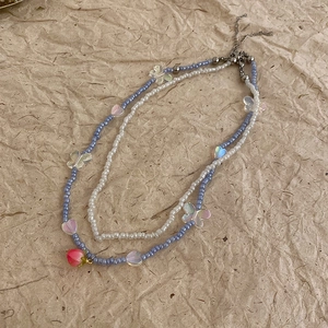 Detailed close-up of double-layered beaded necklace with strawberry and butterfly charms