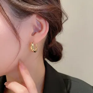 Boucles d'oreilles créoles torsadées dorées à l'or 18 carats portées par un mannequin chic