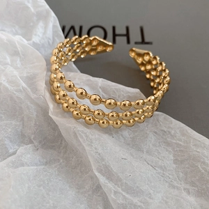 Detail of gold triple-layered beaded open cuff bracelet with textured metallic surface