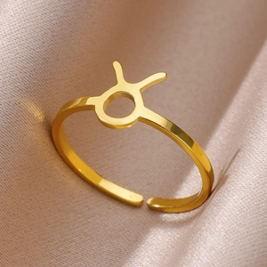 Macro shot of gold Taurus zodiac symbol open ring on premium silk fabric background