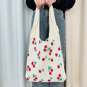 Close-up of cream knit tote bag featuring red cherry pattern and thick knitted texture