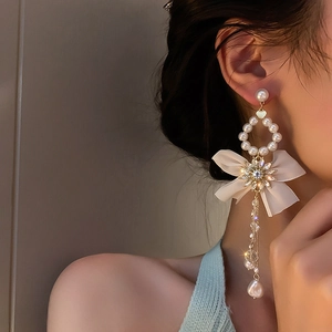 Close-up of asymmetric bow tassel earrings with crystals and pearls on model