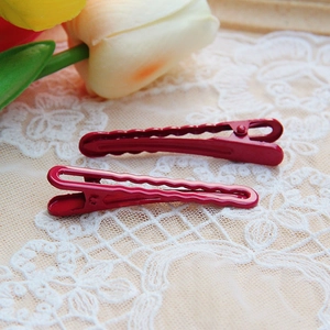 Close-up of red electroplated metal hair clips with wavy edges on white floral lace