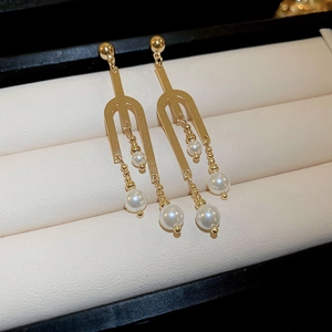 Macro detail of golden U-shaped earrings with cascading white pearls on jewelry display