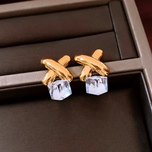 Close-up of golden X-shaped earrings with clear cube crystal drop on dark background