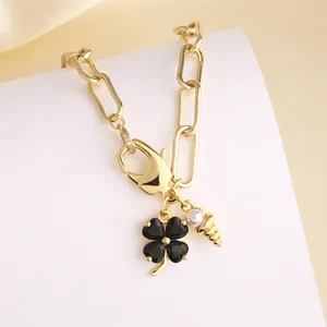 Gouden ketting met zwart klavertje vier, parel en schelphanger in een warm licht getoond