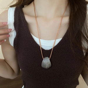 Detailed close-up of a silver shell pendant on a brown braided cord worn by a model