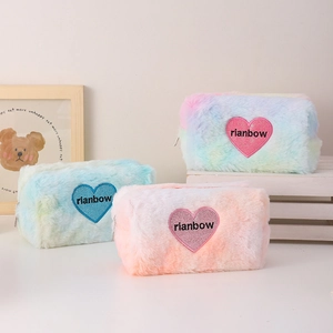 Three gradient plush makeup bags with rainbow heart patches on a minimalist white table