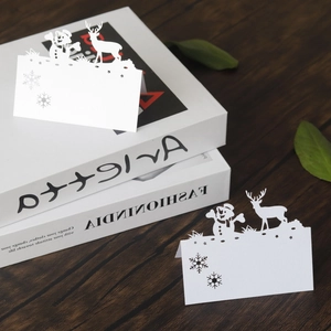 Laser-cut white snowman and reindeer Christmas place cards on a wooden table setup