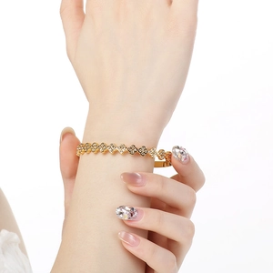 Detail of a gold clover bracelet with white crystals on a model's wrist against white