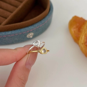 Close-up of gold and silver heart-shaped rings with zircon inlay held by hand