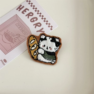 Detailed embroidery texture of a cartoon cat badge holding a baguette on a desk