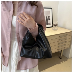 Minimalist soft black PU leather handbag with natural folds held by a model in a casual setting