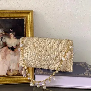 Handmade woven straw beach bag with pearl chain and seashell charms on a book